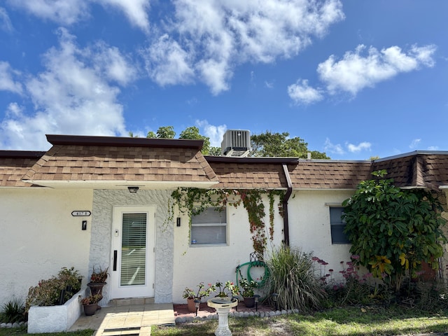 view of front of property with stucco siding, roof with shingles, and mansard roof