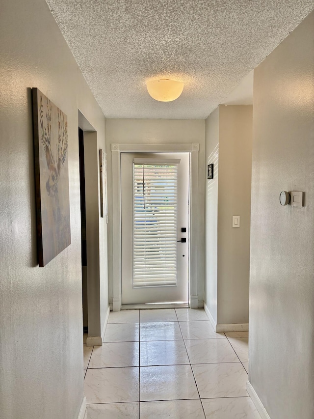 doorway to outside featuring baseboards, a textured ceiling, and light tile patterned flooring