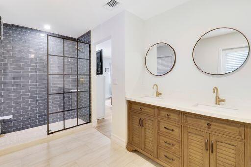 bathroom featuring double vanity, walk in shower, a sink, and visible vents