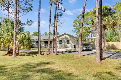 rear view of property featuring driveway, fence, an attached carport, and a lawn