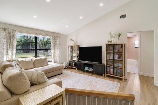 living area with recessed lighting, visible vents, light wood-style floors, high vaulted ceiling, and baseboards