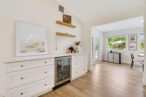 bar featuring beverage cooler, baseboards, vaulted ceiling, light wood-type flooring, and a bar