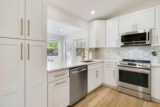 kitchen featuring white cabinets, appliances with stainless steel finishes, light countertops, and a sink