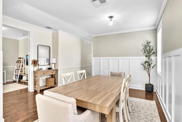 dining room with crown molding, wainscoting, visible vents, and dark wood finished floors