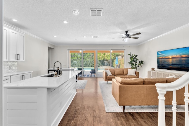 living area with a ceiling fan, visible vents, wood finished floors, and ornamental molding