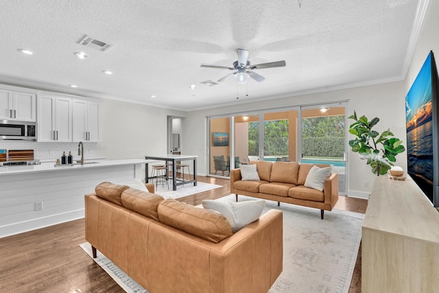 living area with a textured ceiling, wood finished floors, visible vents, baseboards, and ornamental molding