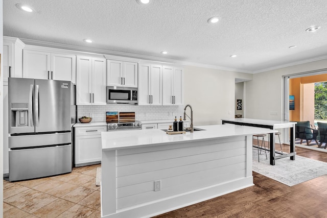 kitchen featuring appliances with stainless steel finishes, ornamental molding, light countertops, white cabinetry, and a sink