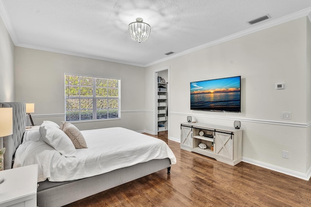 bedroom featuring visible vents, baseboards, wood finished floors, an inviting chandelier, and crown molding