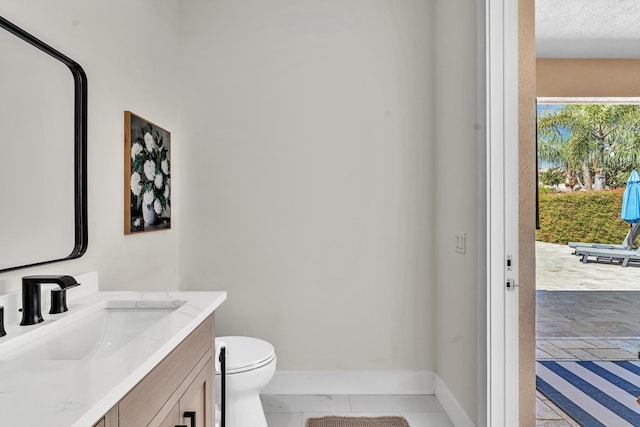 bathroom with a textured ceiling, vanity, toilet, and baseboards