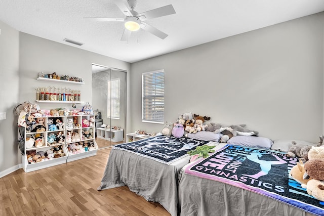 bedroom with a textured ceiling, ceiling fan, visible vents, light wood-style floors, and a closet