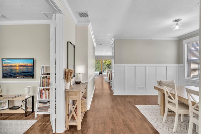 corridor featuring visible vents, a wainscoted wall, ornamental molding, wood finished floors, and a textured ceiling