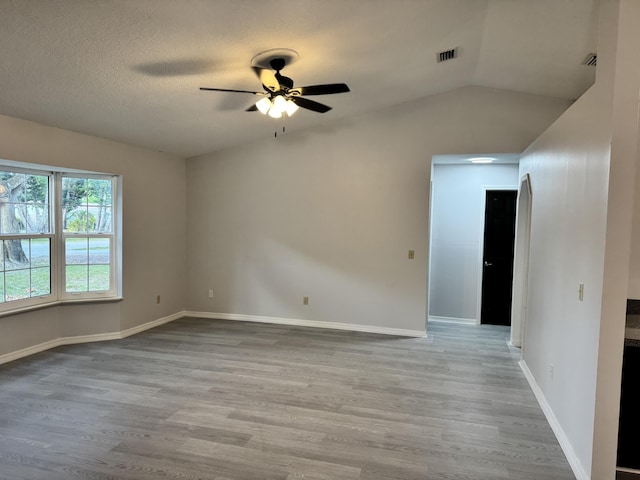 unfurnished room featuring wood finished floors, vaulted ceiling, baseboards, visible vents, and a ceiling fan