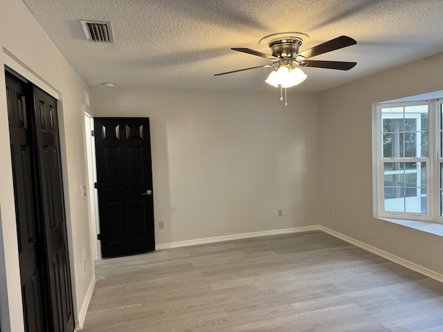 spare room featuring a textured ceiling, visible vents, ceiling fan, and light wood-type flooring