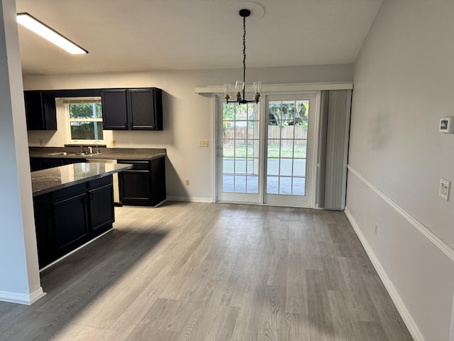 kitchen with dark stone countertops, a chandelier, light wood-style floors, dark cabinetry, and baseboards