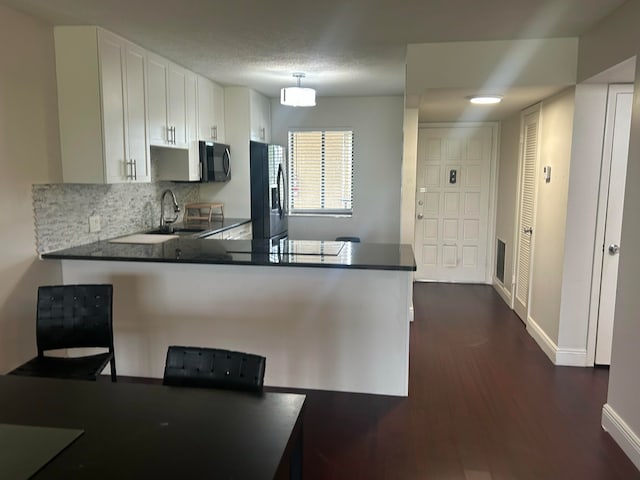 kitchen with stainless steel refrigerator with ice dispenser, tasteful backsplash, a sink, black microwave, and a peninsula