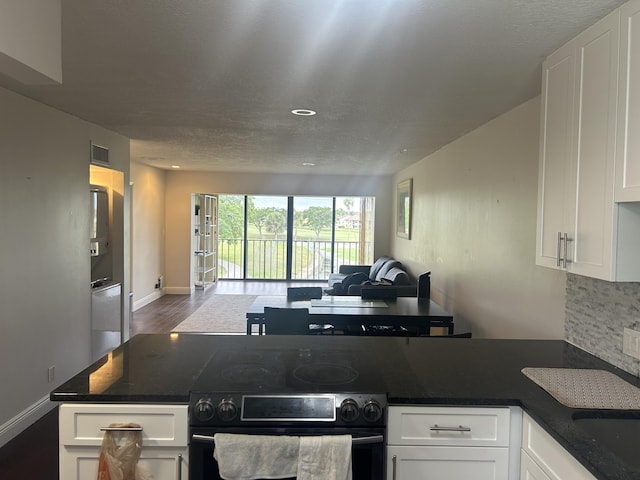 kitchen with black electric range, white cabinets, and backsplash