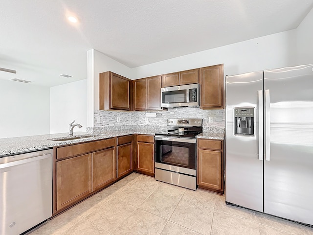 kitchen featuring stainless steel appliances, decorative backsplash, a sink, and light stone countertops