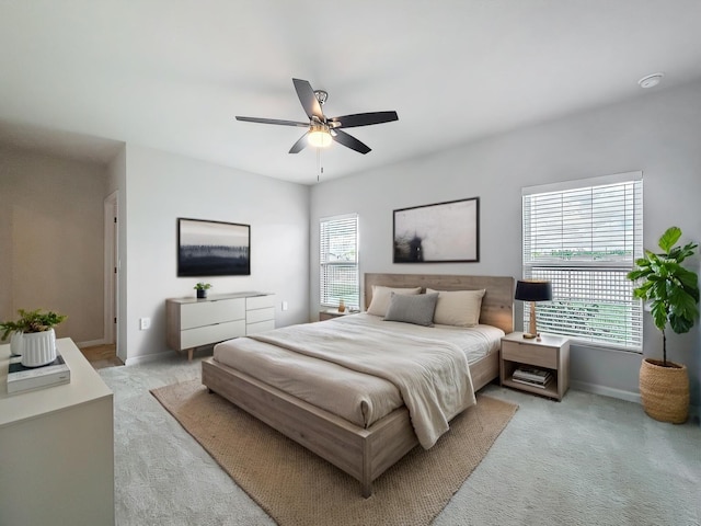 bedroom with light carpet, ceiling fan, multiple windows, and baseboards