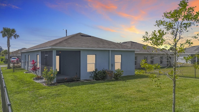 rear view of house featuring a lawn, a sunroom, roof with shingles, fence private yard, and stucco siding