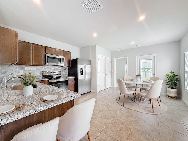 kitchen featuring light stone counters, tasteful backsplash, visible vents, appliances with stainless steel finishes, and a sink