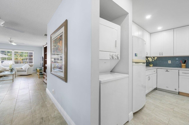 kitchen featuring stacked washer and clothes dryer, light countertops, open floor plan, white cabinetry, and white dishwasher