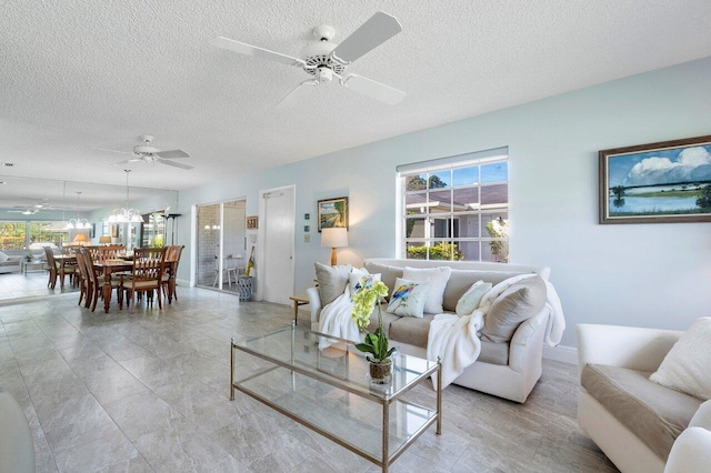 living area with ceiling fan with notable chandelier, a textured ceiling, and baseboards