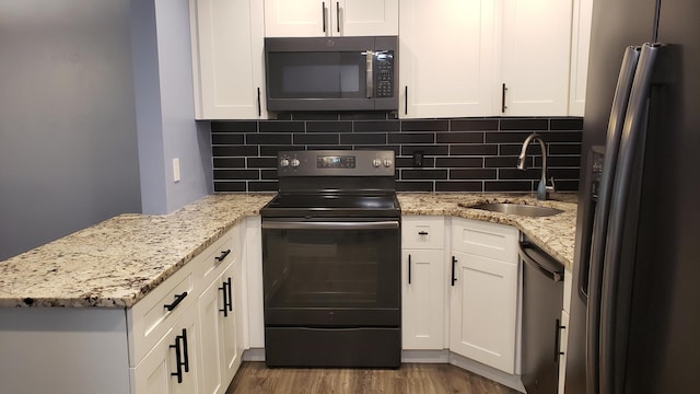 kitchen with light stone counters, stainless steel appliances, a sink, white cabinets, and decorative backsplash