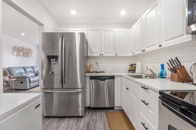 kitchen with stainless steel appliances, white cabinets, light countertops, light wood-type flooring, and backsplash