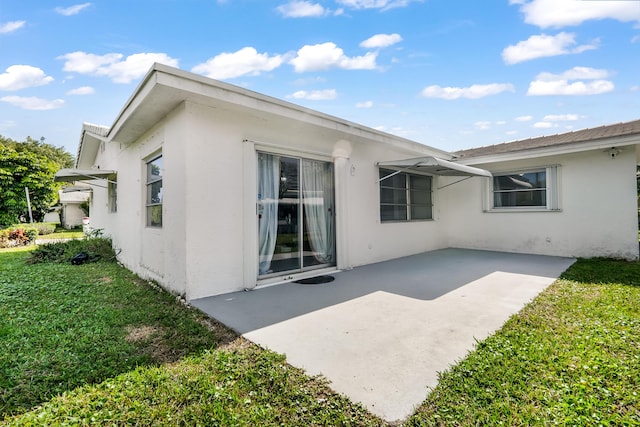 rear view of property featuring stucco siding, a yard, and a patio