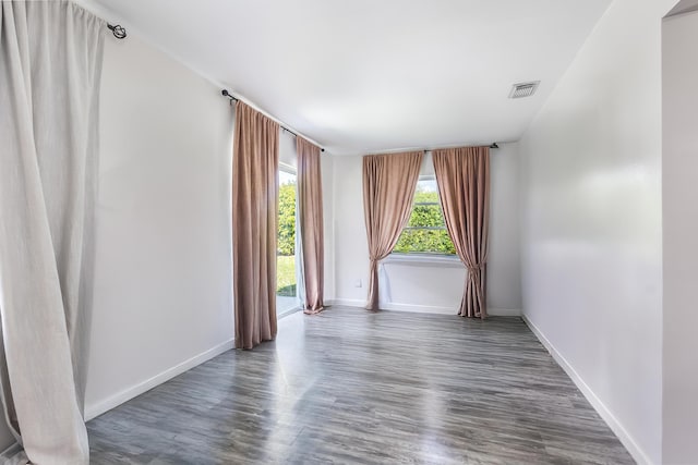 empty room with dark wood-style flooring, visible vents, and baseboards