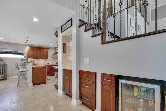 kitchen featuring wine cooler, light countertops, wall chimney range hood, backsplash, and recessed lighting