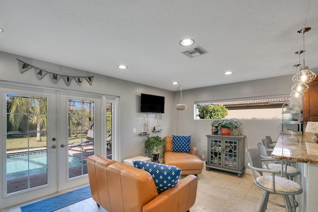 living area with a textured ceiling, recessed lighting, visible vents, french doors, and stone finish flooring