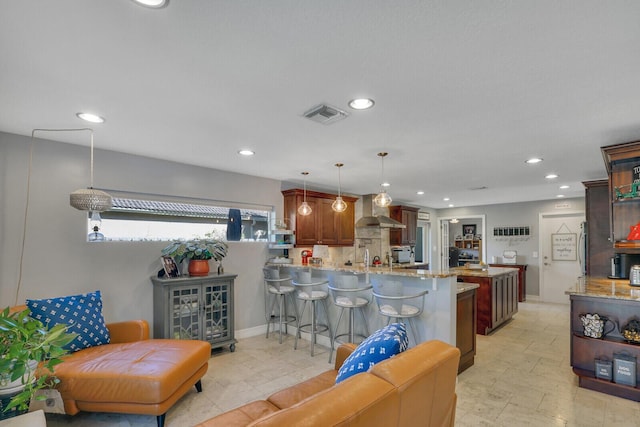 kitchen featuring visible vents, wall chimney exhaust hood, a breakfast bar, a peninsula, and light stone countertops