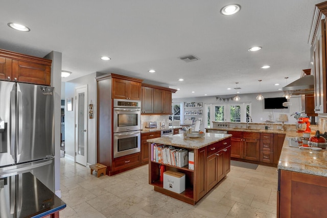 kitchen featuring a peninsula, appliances with stainless steel finishes, range hood, and stone tile floors