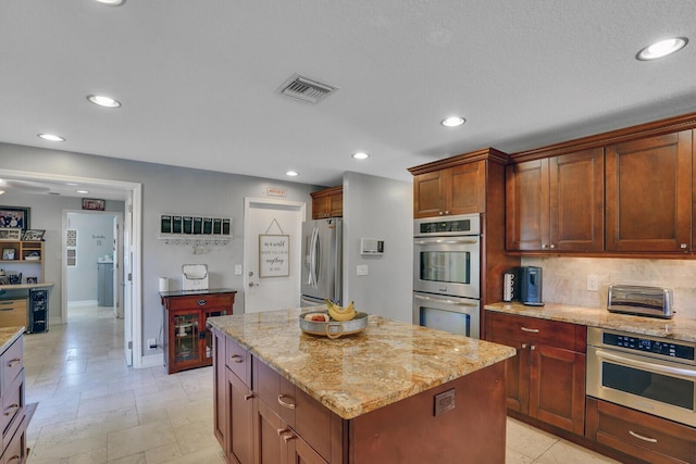 kitchen featuring light stone counters, recessed lighting, stainless steel appliances, a kitchen island, and visible vents