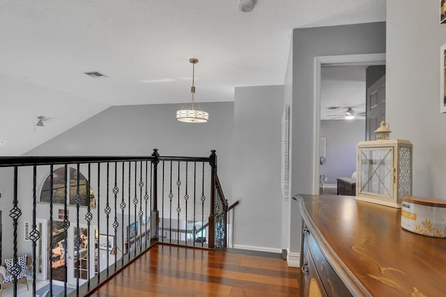 hallway featuring a textured ceiling, wood finished floors, an upstairs landing, visible vents, and baseboards