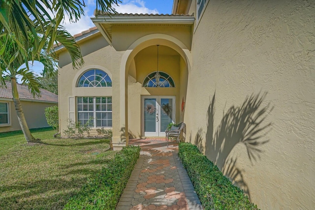 view of exterior entry with french doors, a yard, and stucco siding