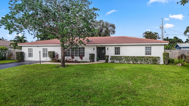 view of front of home with stucco siding, a front yard, fence, driveway, and a tiled roof