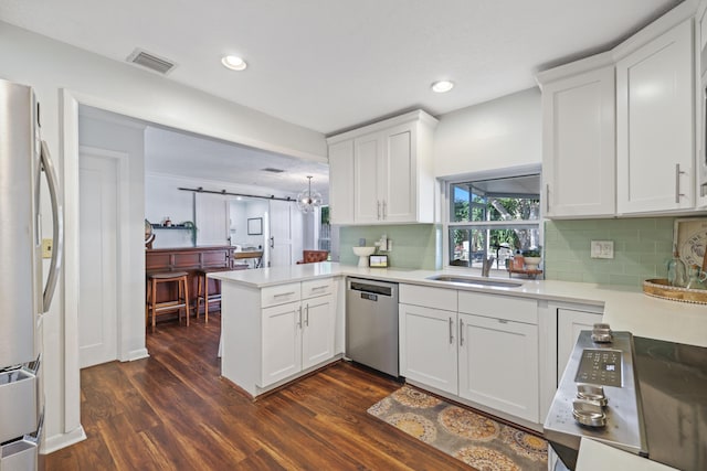 kitchen with a barn door, a peninsula, stainless steel appliances, a sink, and white cabinetry