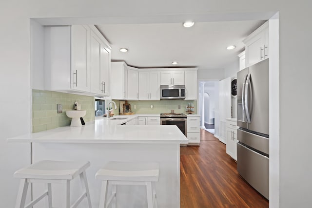 kitchen with a peninsula, white cabinetry, a kitchen breakfast bar, light countertops, and appliances with stainless steel finishes