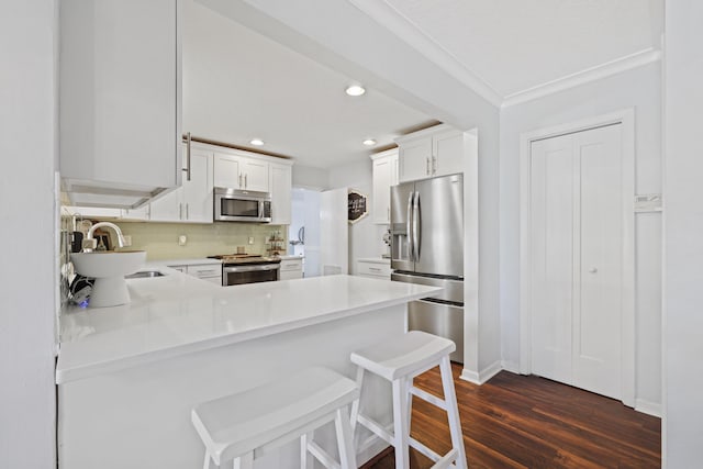 kitchen featuring appliances with stainless steel finishes, a peninsula, light countertops, white cabinetry, and a sink