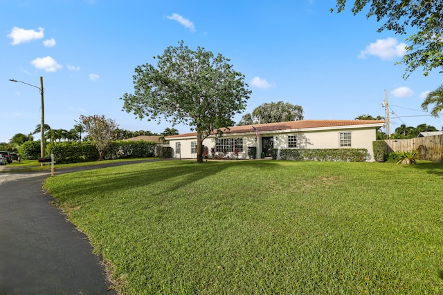 ranch-style home featuring a front yard, fence, a tiled roof, and stucco siding