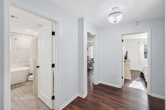 corridor with dark wood-style floors, a chandelier, visible vents, and baseboards