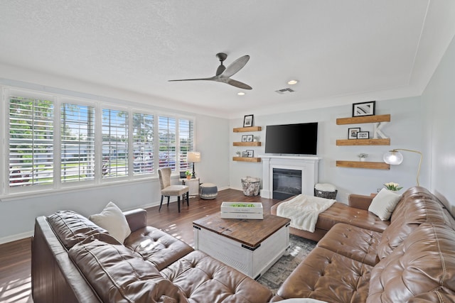 living area with dark wood-style floors, a glass covered fireplace, visible vents, and baseboards