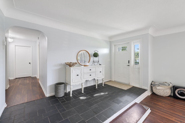 entrance foyer featuring arched walkways, dark wood-style flooring, and baseboards