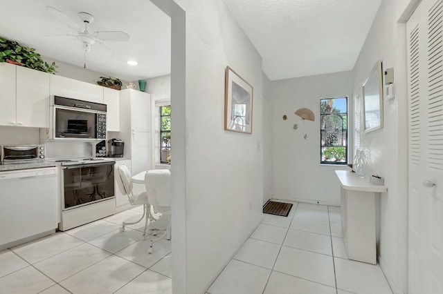 kitchen with white appliances, light tile patterned floors, white cabinets, light countertops, and a wealth of natural light