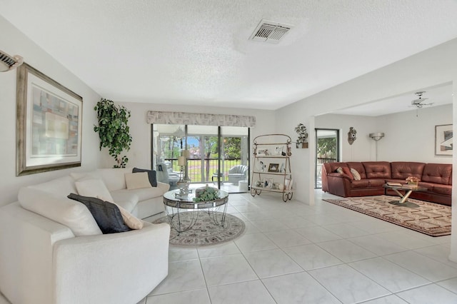 living area with a textured ceiling, ceiling fan, light tile patterned flooring, and visible vents