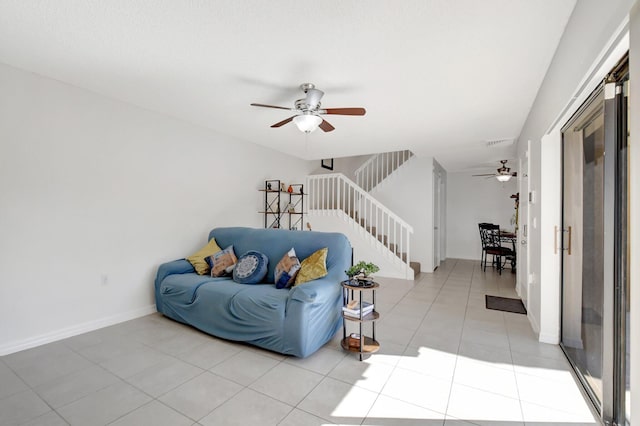 living room featuring a ceiling fan, baseboards, visible vents, light tile patterned flooring, and stairway