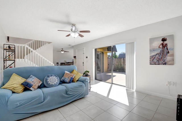 living room with a textured ceiling, light tile patterned floors, baseboards, ceiling fan, and stairway