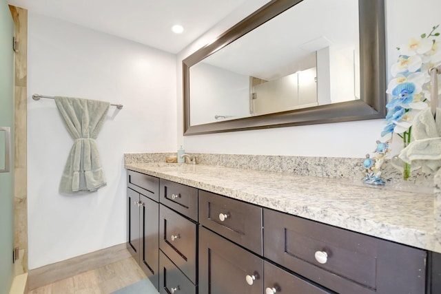 bathroom with a shower with shower door, baseboards, vanity, and wood finished floors